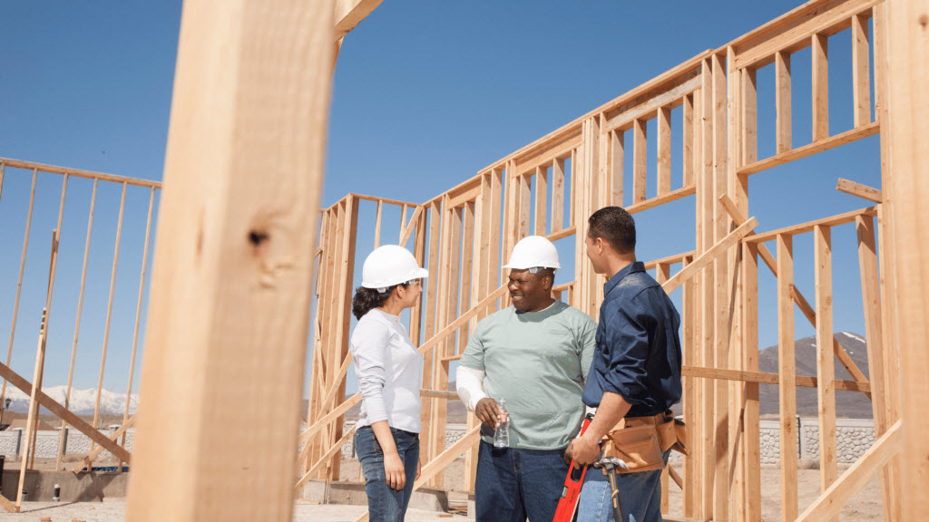 Builders in hard hats discussing timber house framing at a construction site