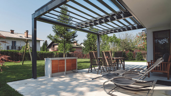 Black steel-frame pergola over a paved patio with an outdoor kitchen and seating